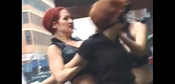  Two lustful lesbians tie their redhead girlfriend to a pole on the street and beat her with a whip